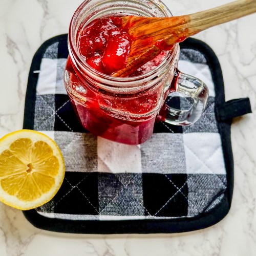 Strawberry compote in a glass mason jar on a hot pad with a lemon next to it