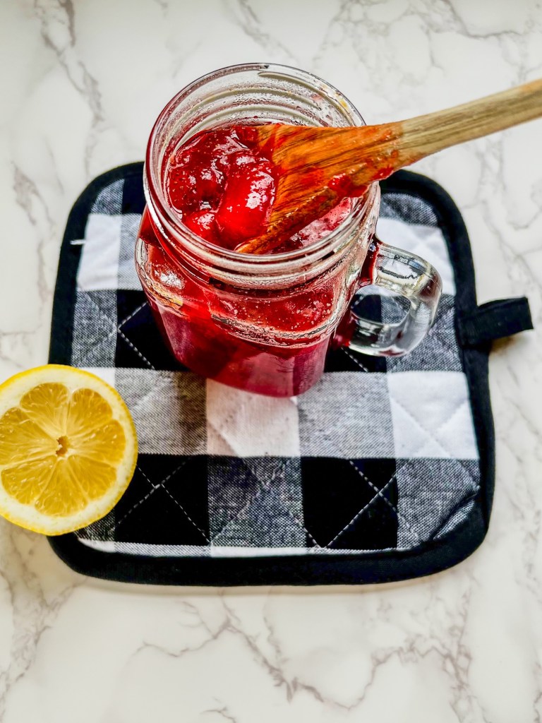Strawberry compote in a glass mason jar on a hot pad with a lemon next to it