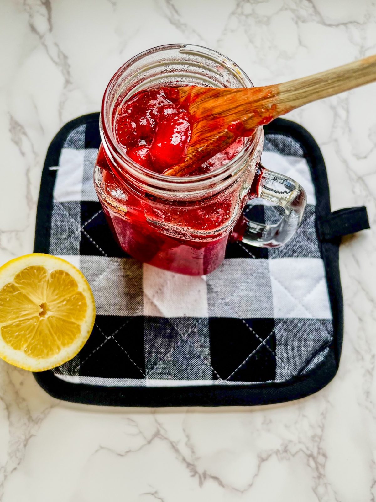 Strawberry compote in a glass mason jar on a hot pad with a lemon next to it