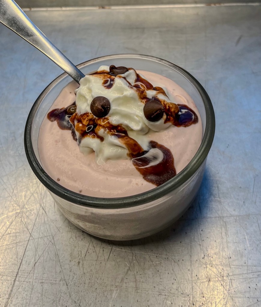 Strawberry mousse in a small dish with whipped cream, chocolate sauce, and chocolate chips on top