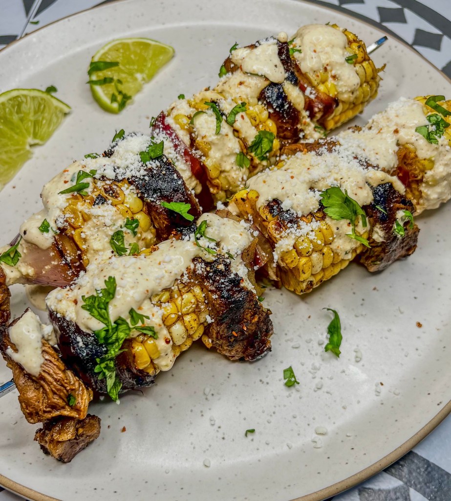 Street corn kabobs on a white plate with some lime wedges off to the side
