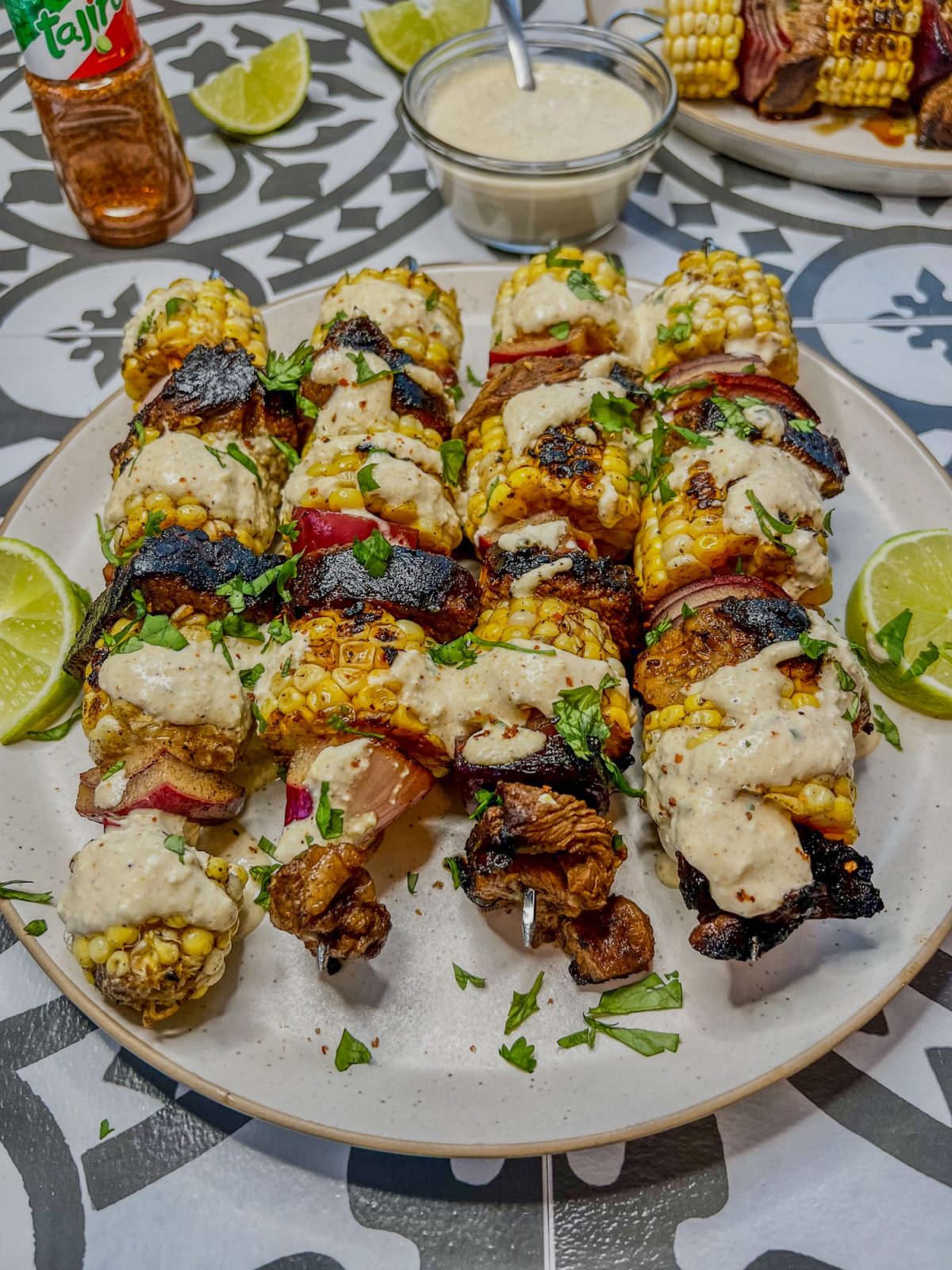 Street Corn Steak Kabobs on a plate with some lime, cilantro, and cotija crema drizzled on them and scattered all around