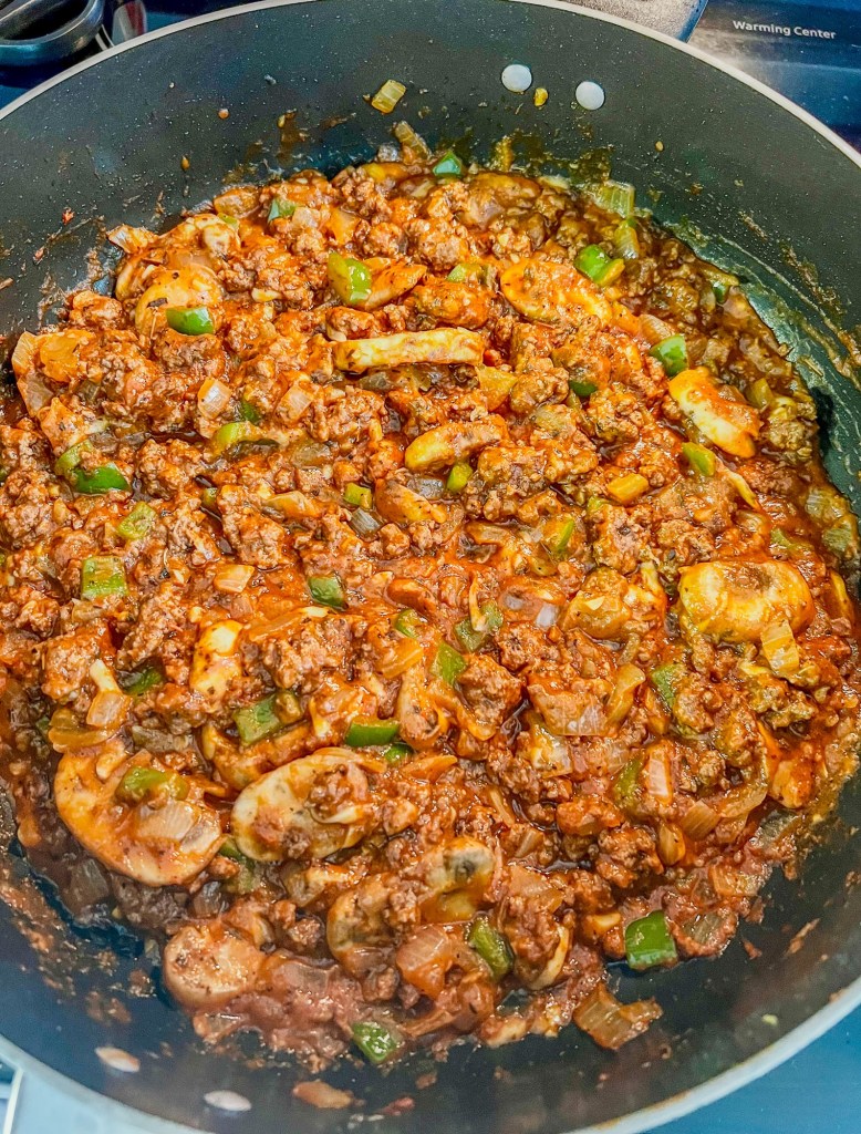 A skillet with snake river farms ground beef, a bunch of veggies, cheese, spices, and pizza sauce in it