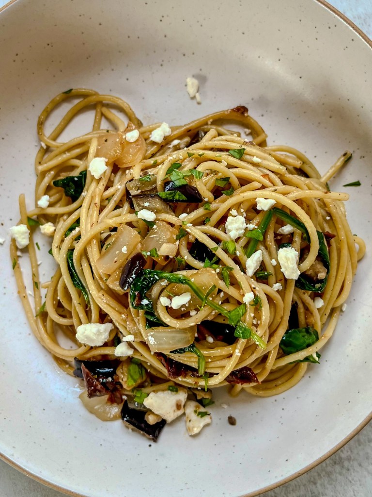 Sun-dried tomato eggplant pasta in a white bowl with some parsley and feta on top