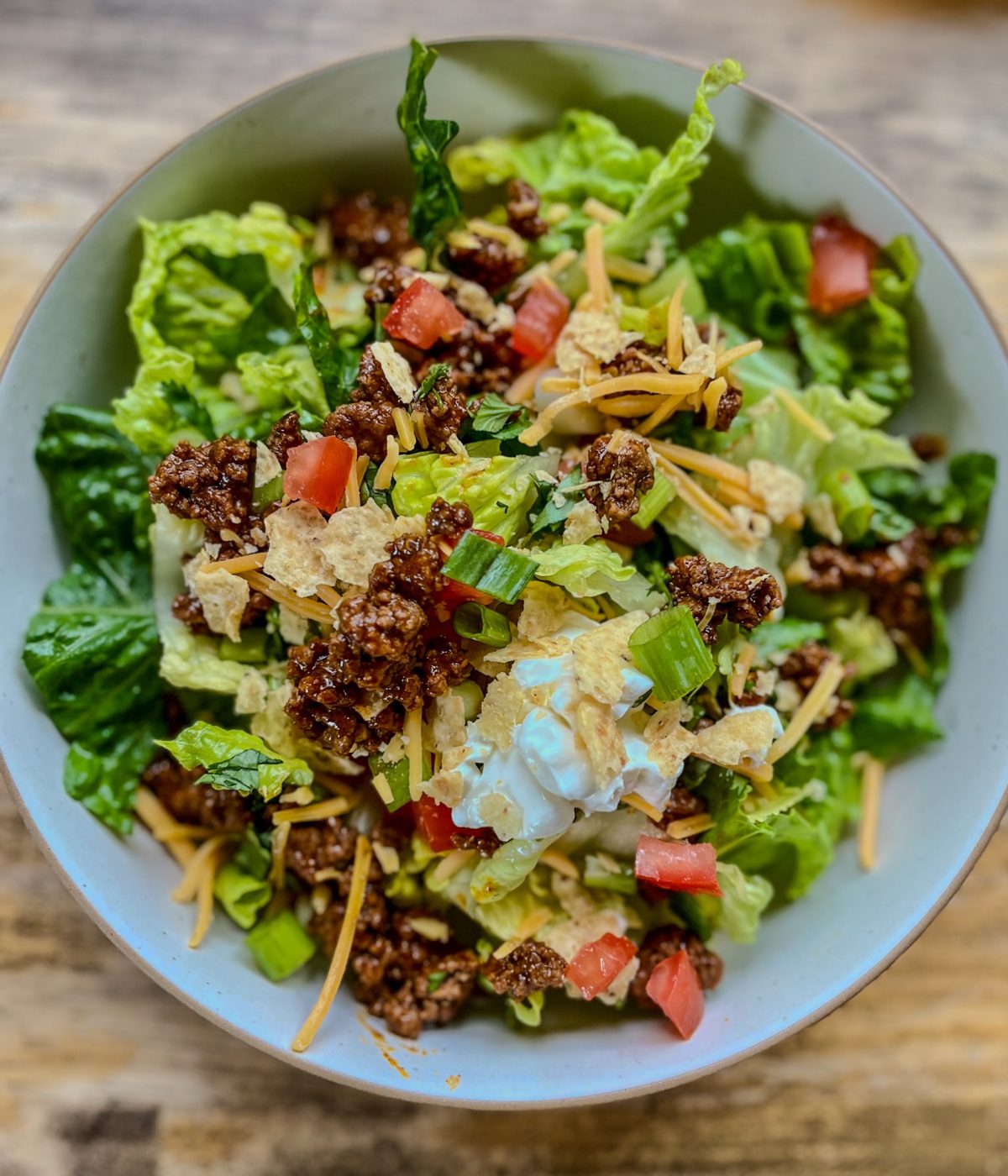 Taco salad in a white bowl with some cheese and sour cream for garnish