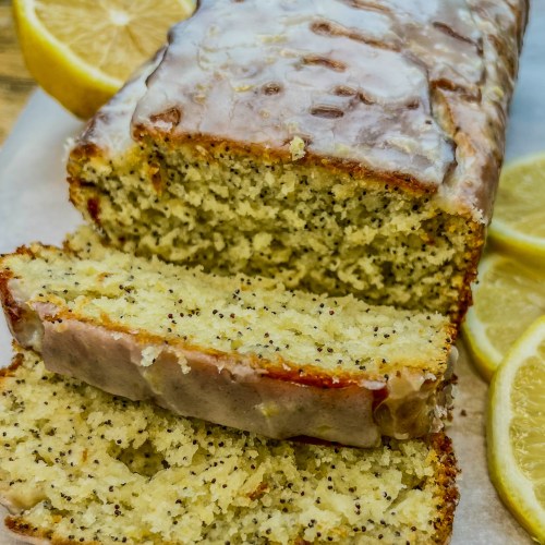 Triple Lemon Poppy Seed Loaf that's been iced and sliced on a cutting board with some sliced lemon nearby