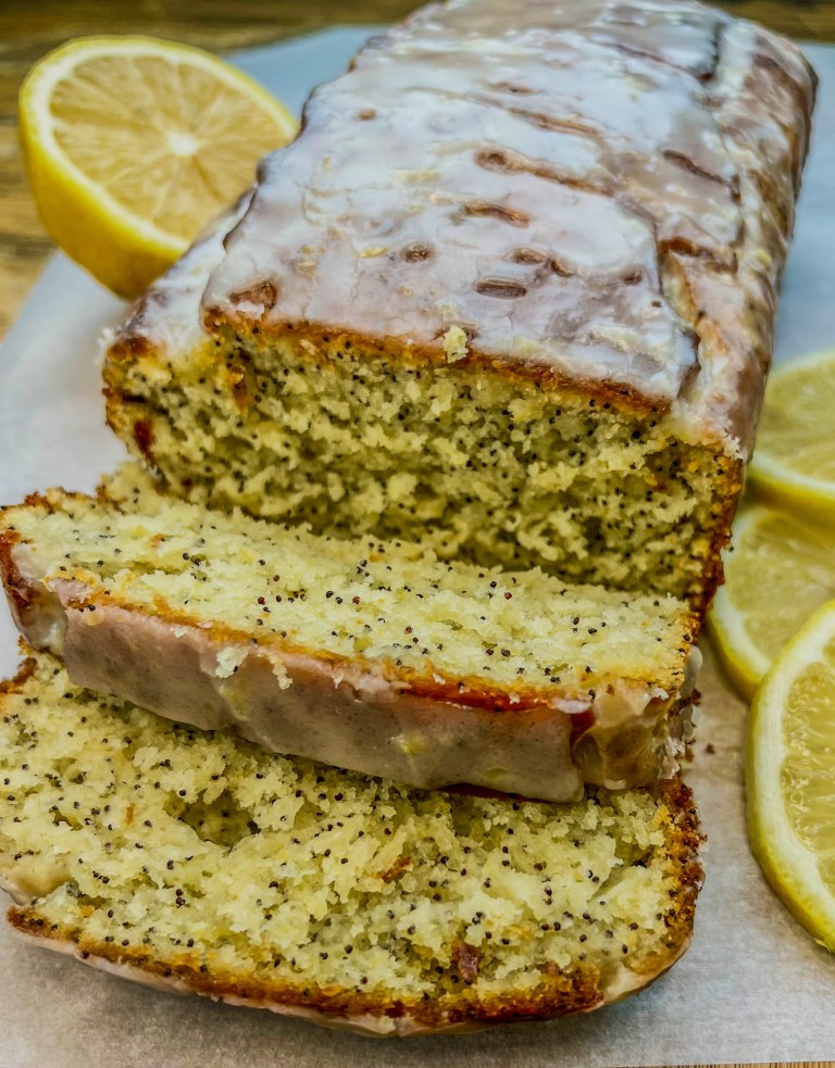 Triple Lemon Poppy Seed Loaf that's been iced and sliced on a cutting board with some sliced lemon nearby