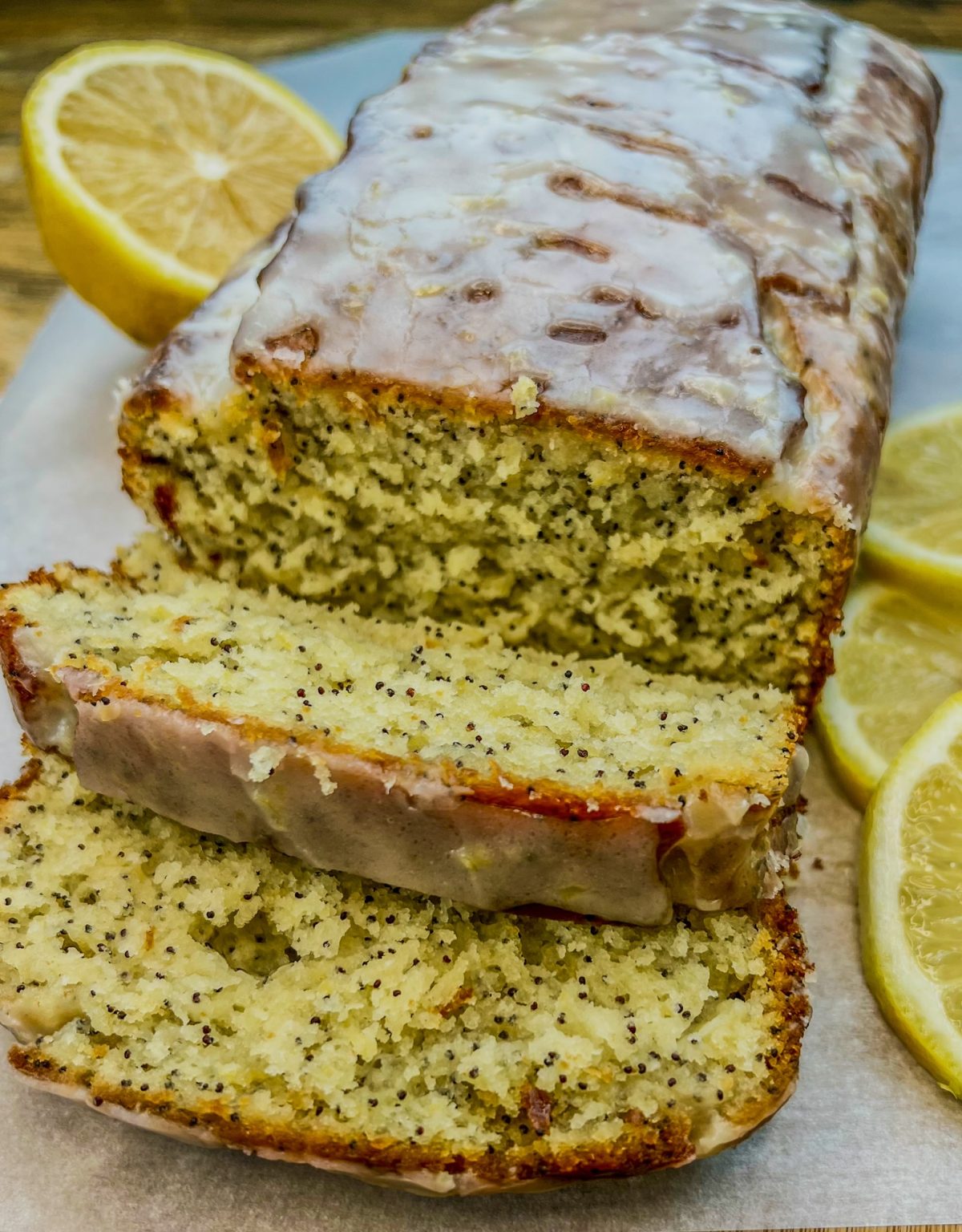 Triple Lemon Poppy Seed Loaf that's been iced and sliced on a cutting board with some sliced lemon nearby