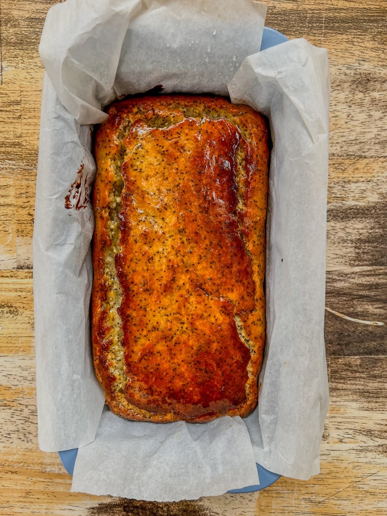 Lemon poppy seed bread in a loaf pan after lemon syrup soak has been brushed onto it