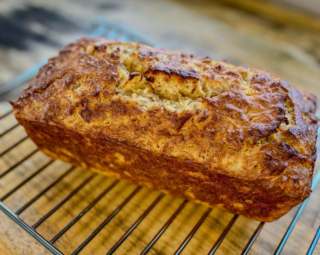 A loaf of tropical banana bread sitting on a cooling rack on a wooden table