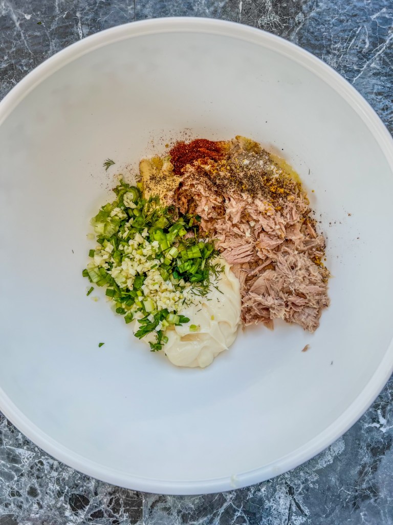Tuna salad ingredients in a bowl before being stirred and chilled