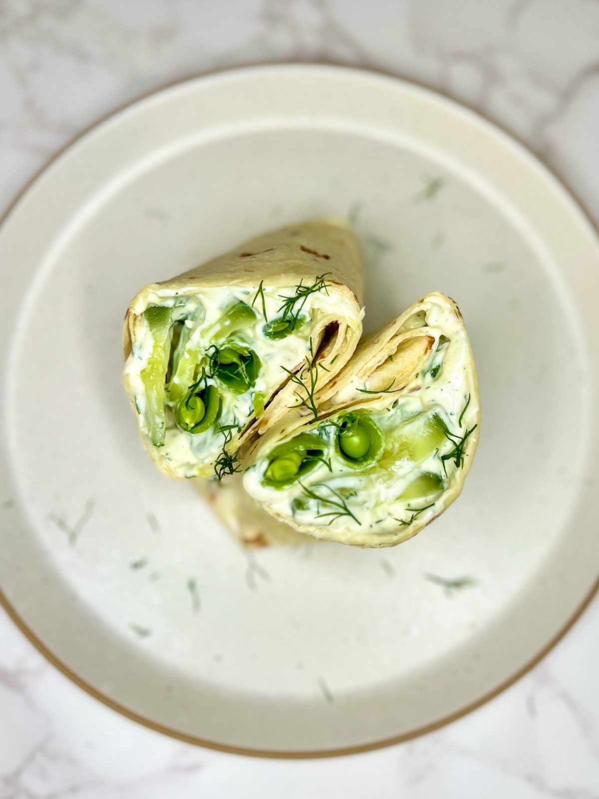 Veggie Wrap with Basil Tzatziki that's been cut in half and garnished with dill on a white plate