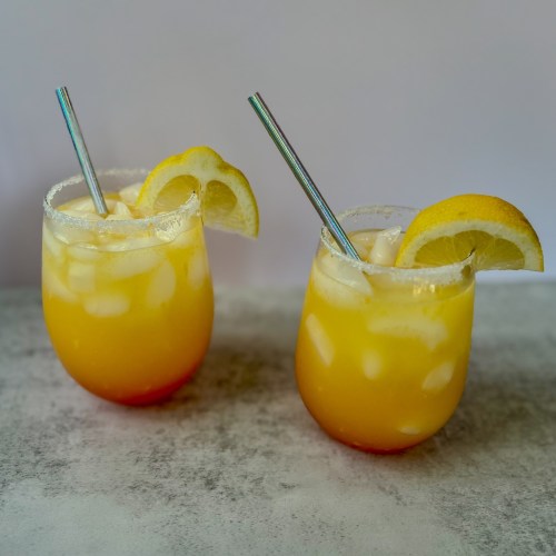Two vodka summer sunrise drinks with lemon wedges for garnish and straws sitting on a countertop