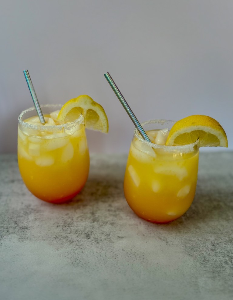Two vodka summer sunrise drinks with lemon wedges for garnish and straws sitting on a countertop