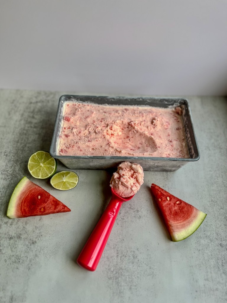 Watermelon Lime Ice Cream that's been scooped on a marble counter with watermelon and lime nearby
