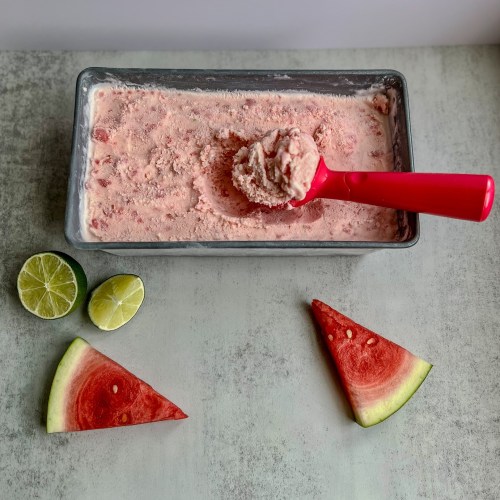 Watermelon Lime Ice Cream that's been scooped, sitting on a marble counter with lime and watermelon nearby