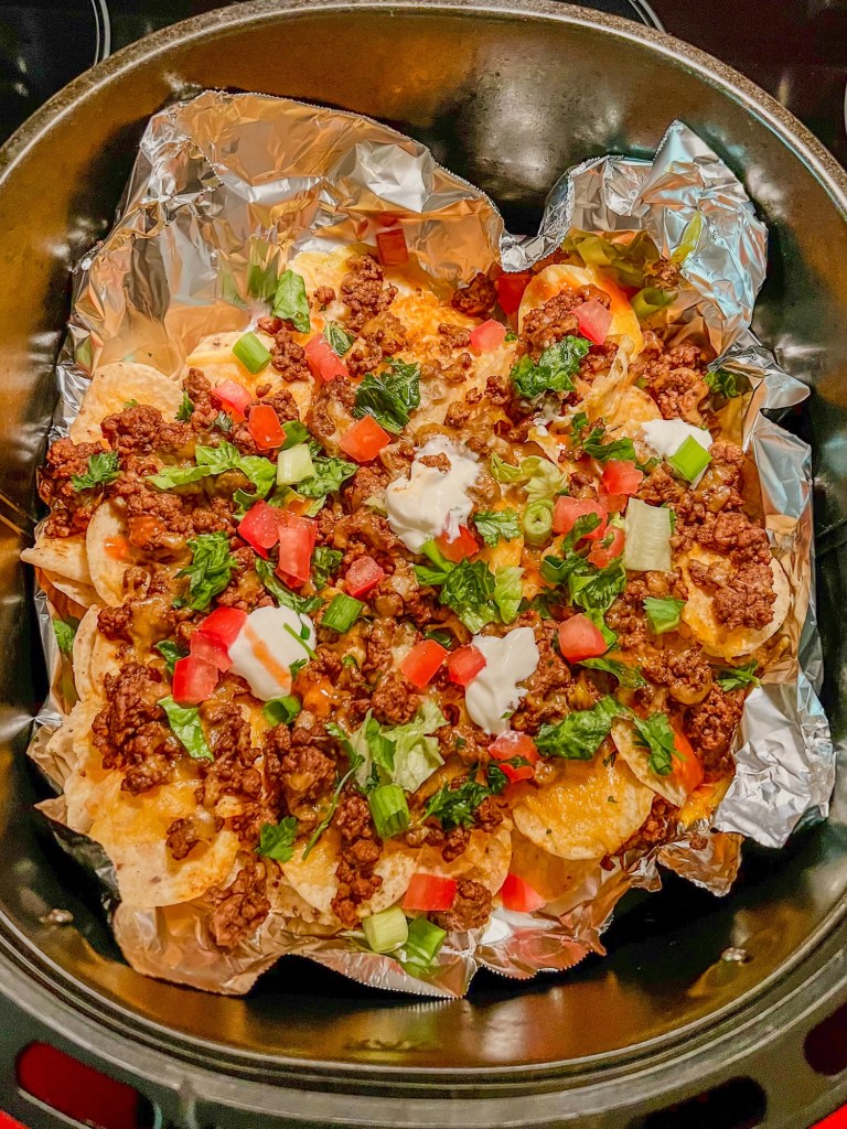 Air fryer nachos with garnishes on top in an air fryer basket