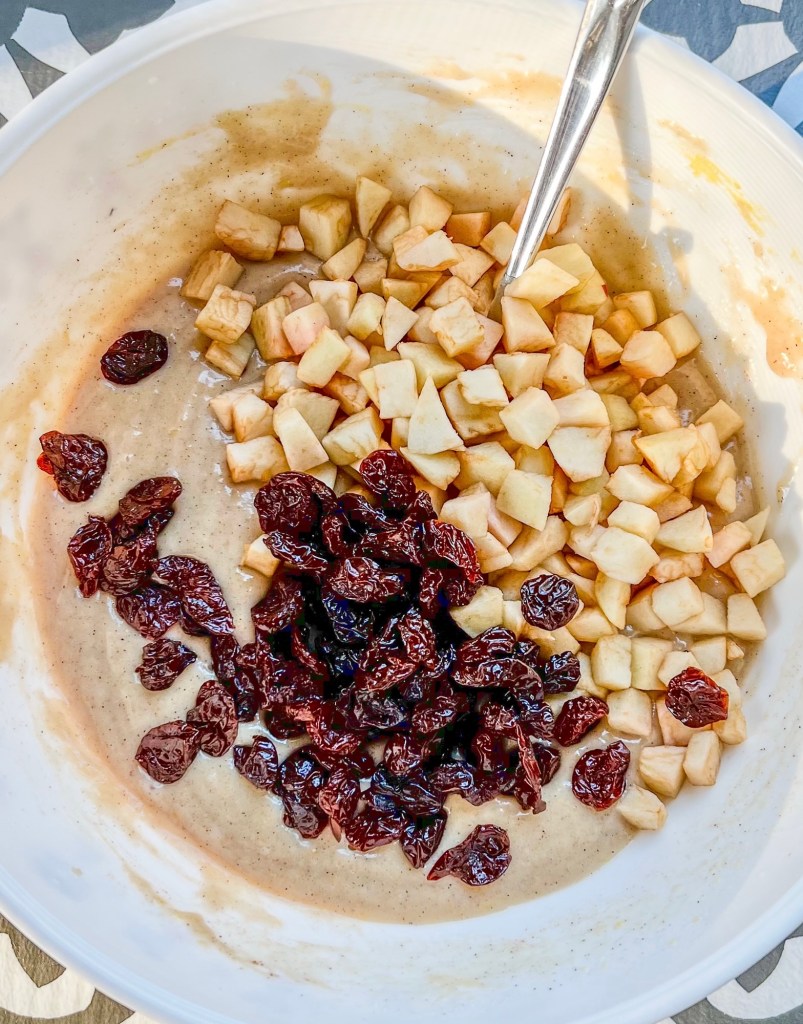 Muffin batter in a large bowl with some dehydrated cherries and freshly diced apples being mixed in