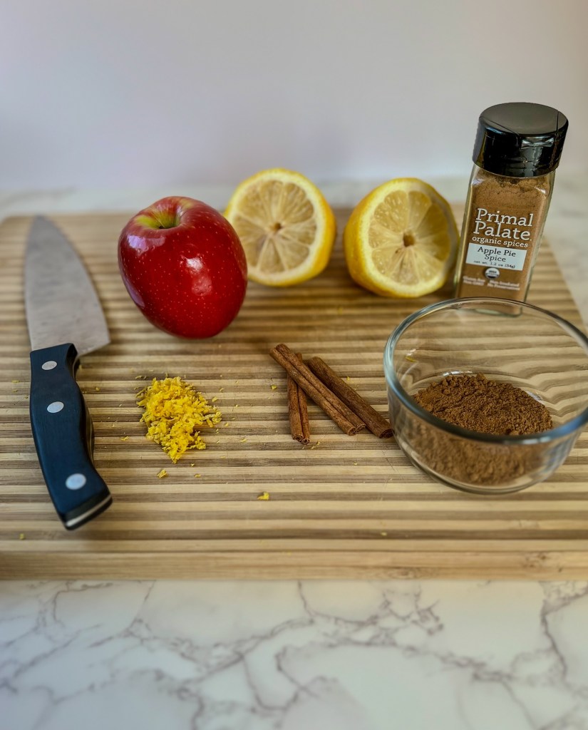 Lemon, spices, cinnamon sticks, apples, zest and a knife on a cutting board