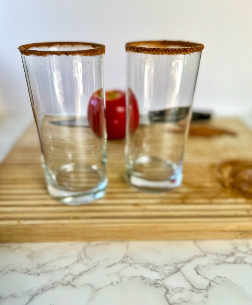 Two glasses with apple pie spice on the rims on a wooden cutting board