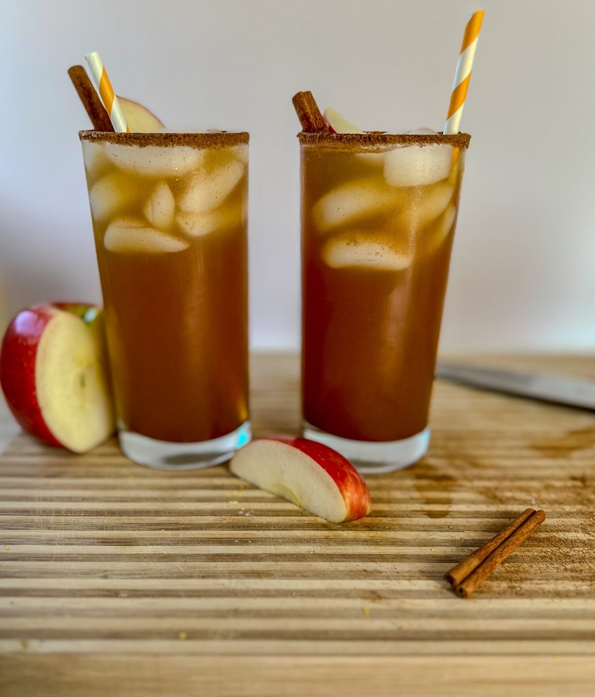 Two apple cider whiskey sours on a wooden cutting board with some spices and apples next to it