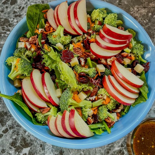 Apple salad in a bowl with some honey balsamic vinaigrette in a dish off to the side