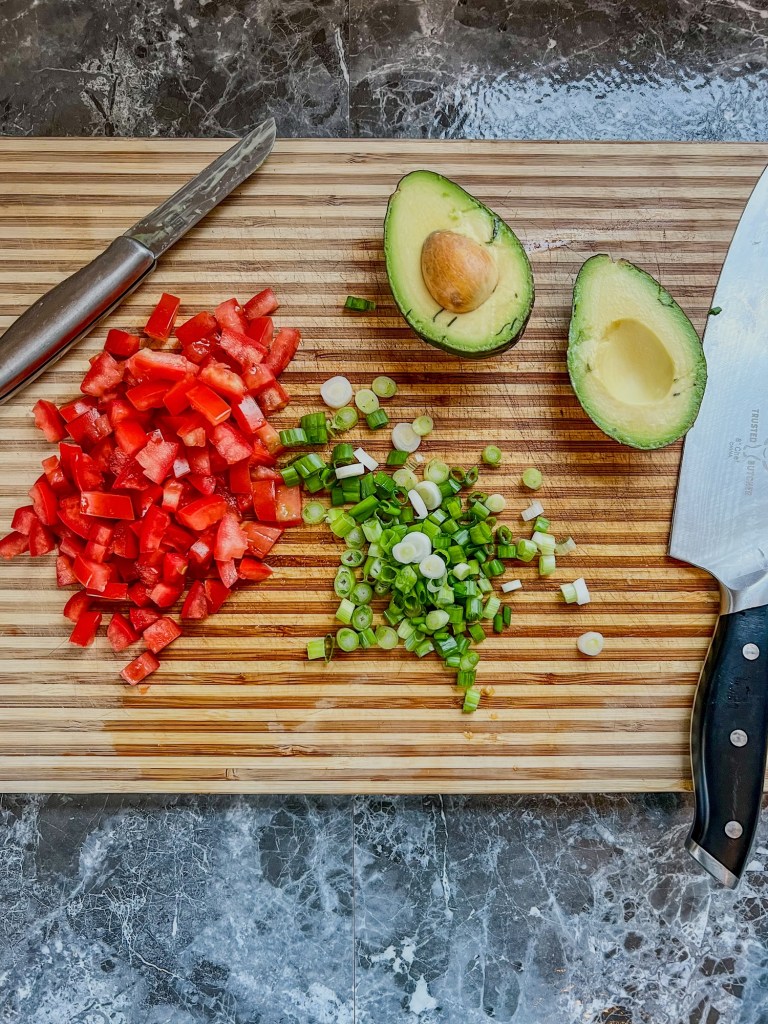 Tomato, green onion, and avocado cut up on a wooden cutting board
