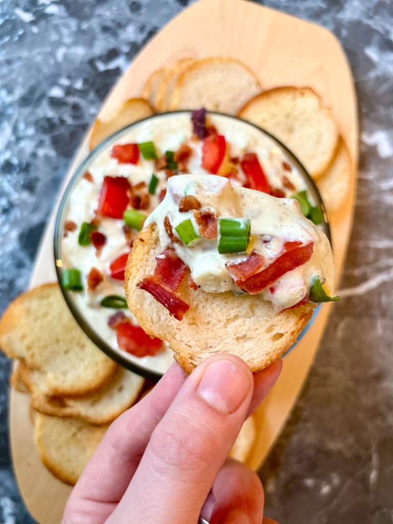 A hand scooping some avocado blt dip with a bagel crisp