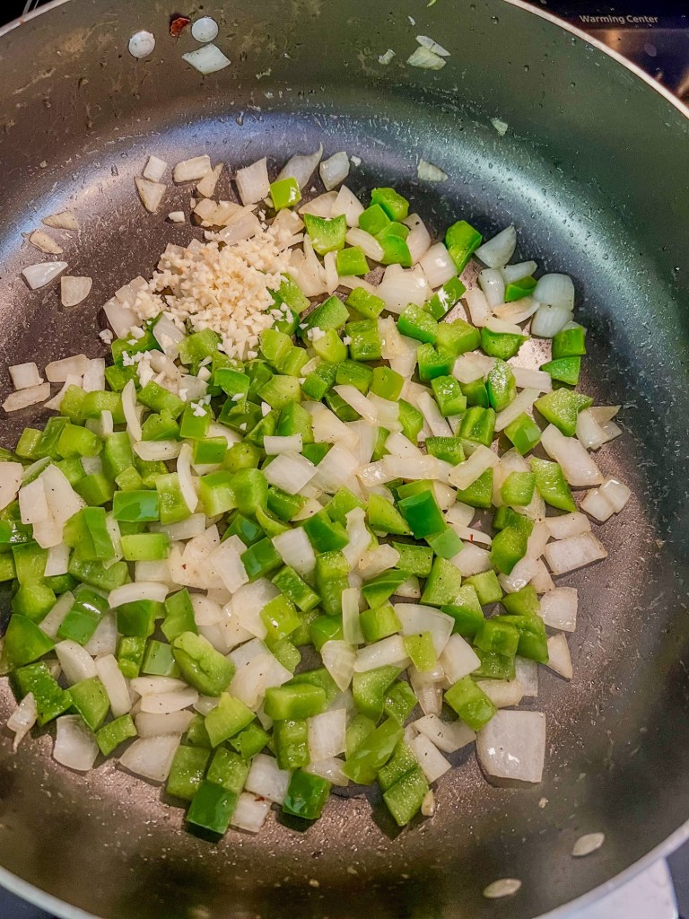 A large skillet filled with green pepper, onion, and garlic, cooking on the stove