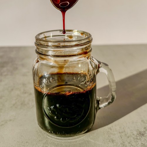 Balsamic glaze in a glass jar with a spoon scooping some out up above it