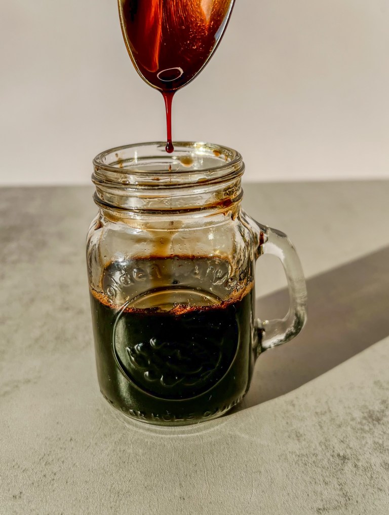 Balsamic glaze in a glass jar with a spoon scooping some out up above it