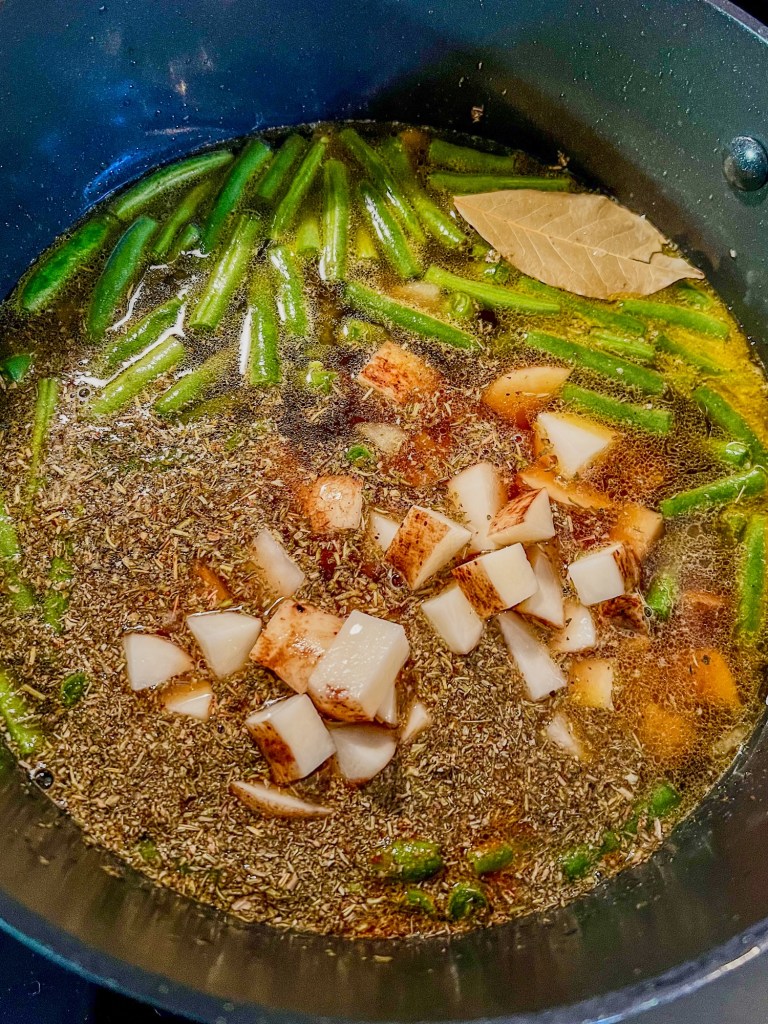 A large stockpot with ingredients for beefy vegetable soup cooking on the stove