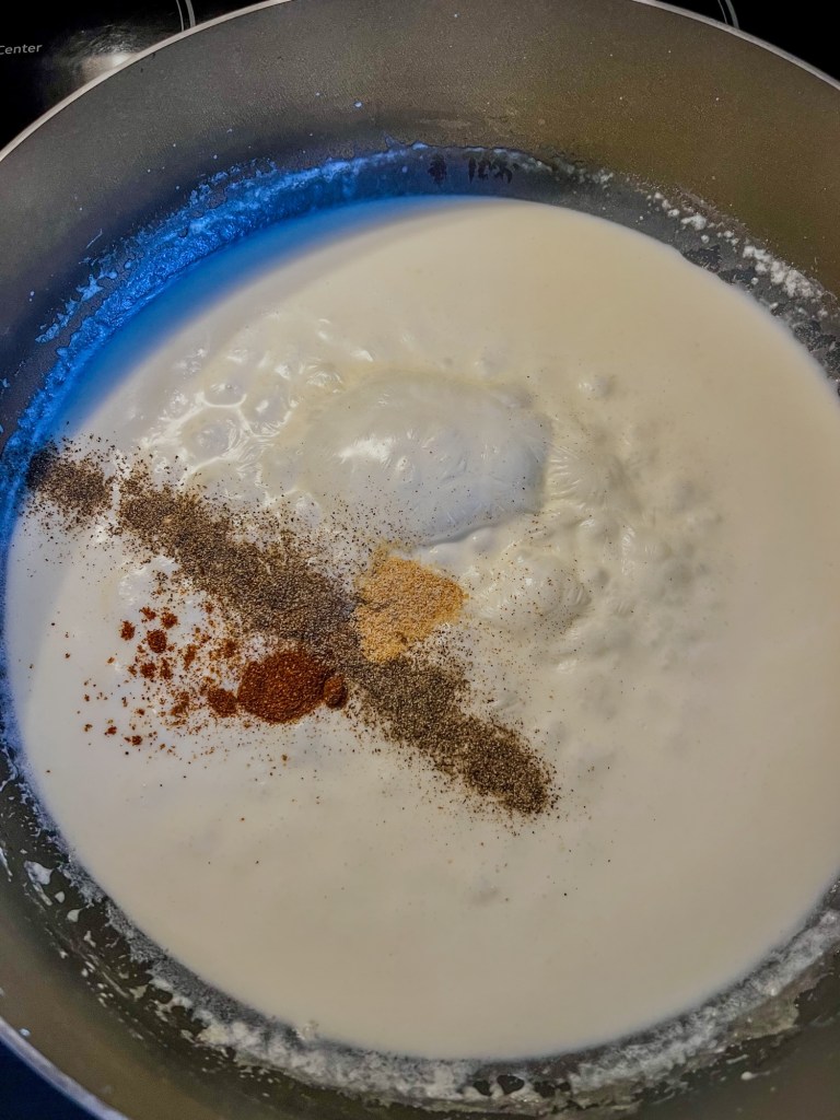 White gravy being made in a skillet with a bunch of seasonings just added in