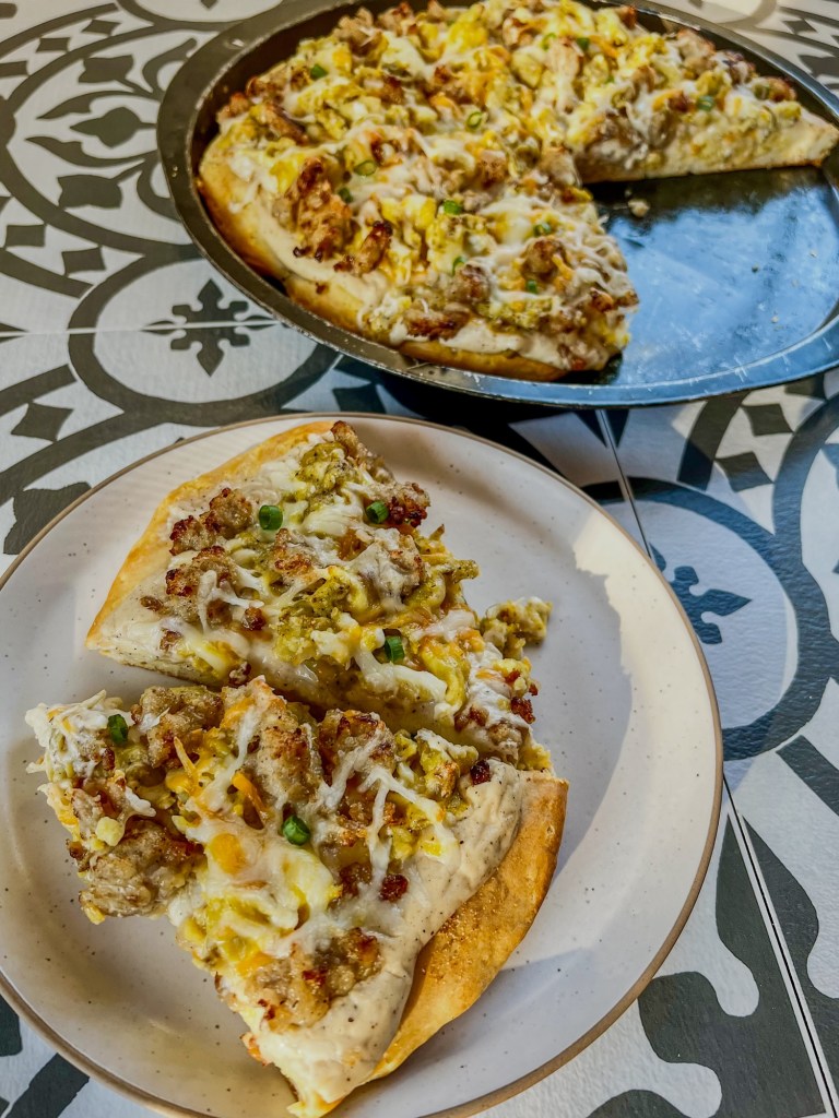 Biscuits and gravy breakfast pizza that's been cut with two slices on a white plate nearby