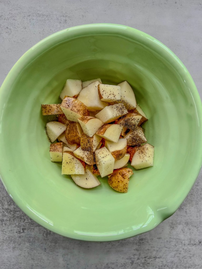 Diced russet potatoes in a bowl with some spices and oil before going into the oven