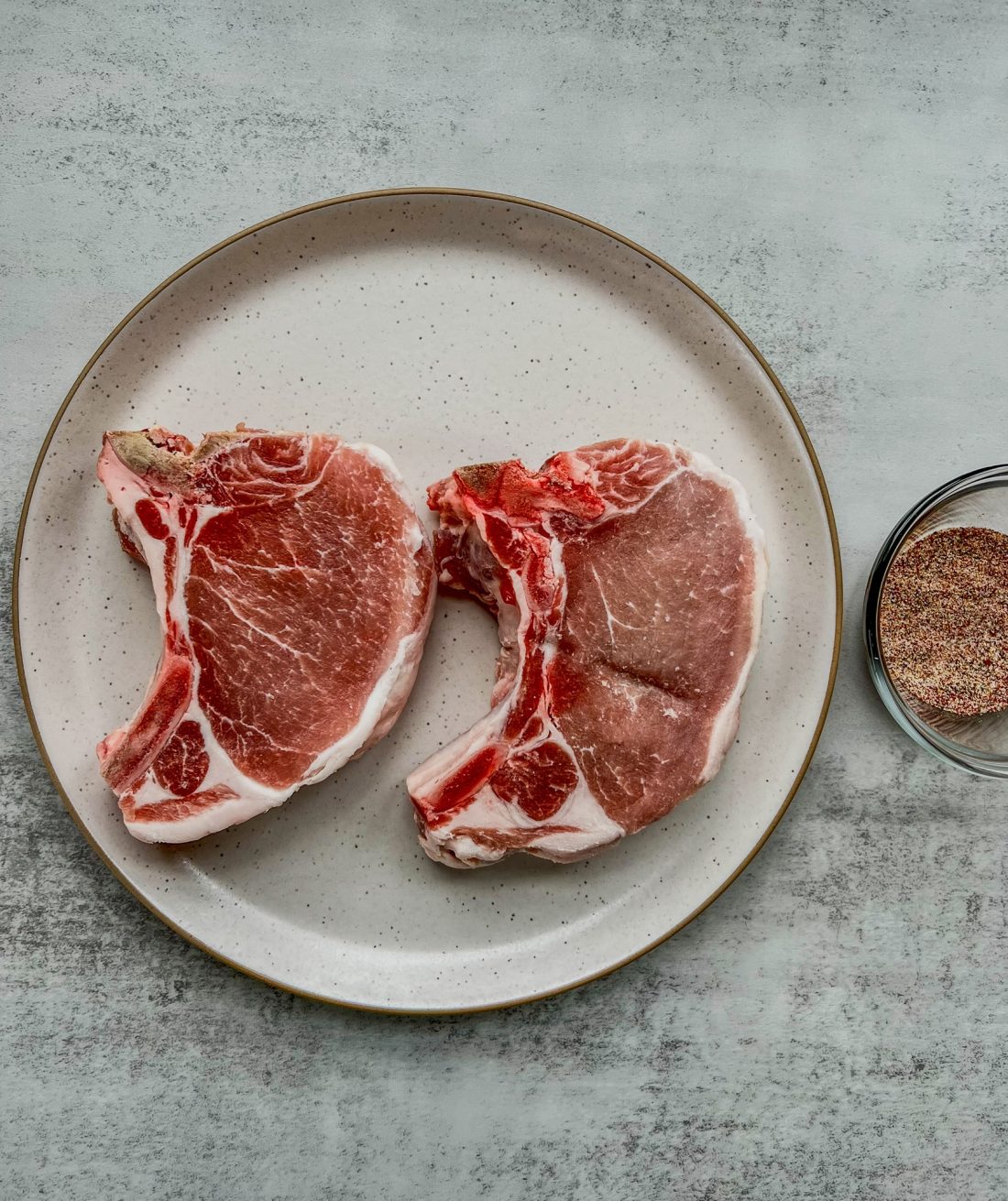 Bone-in pork chops on a plate before being coated in spices and seared