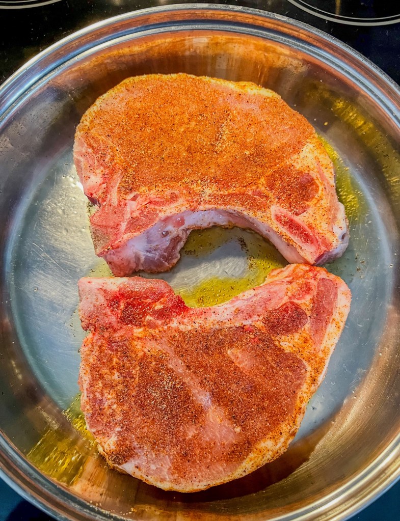 Pork chops getting seared in a stainless-steel skillet