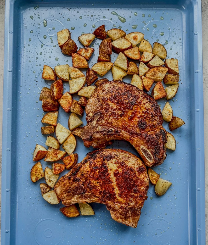Pork chops and diced potatoes on a sheet pan before going into the oven for a second time