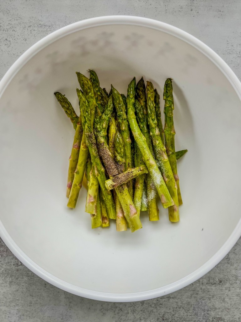 Trimmed asparagus in a bowl with oil and spices