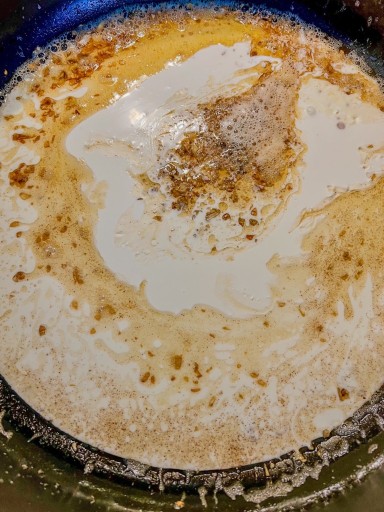 Alfredo sauce being built in a skillet with freshly added heavy cream