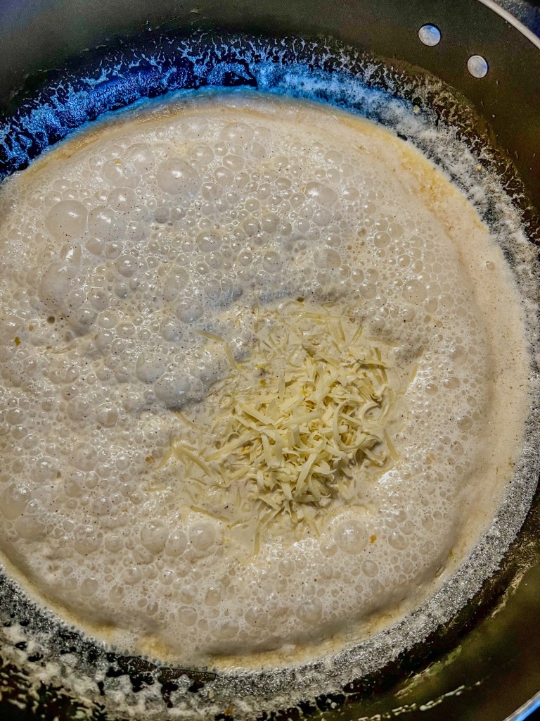 Alfredo sauce in a skillet with freshly added parmesan cheese