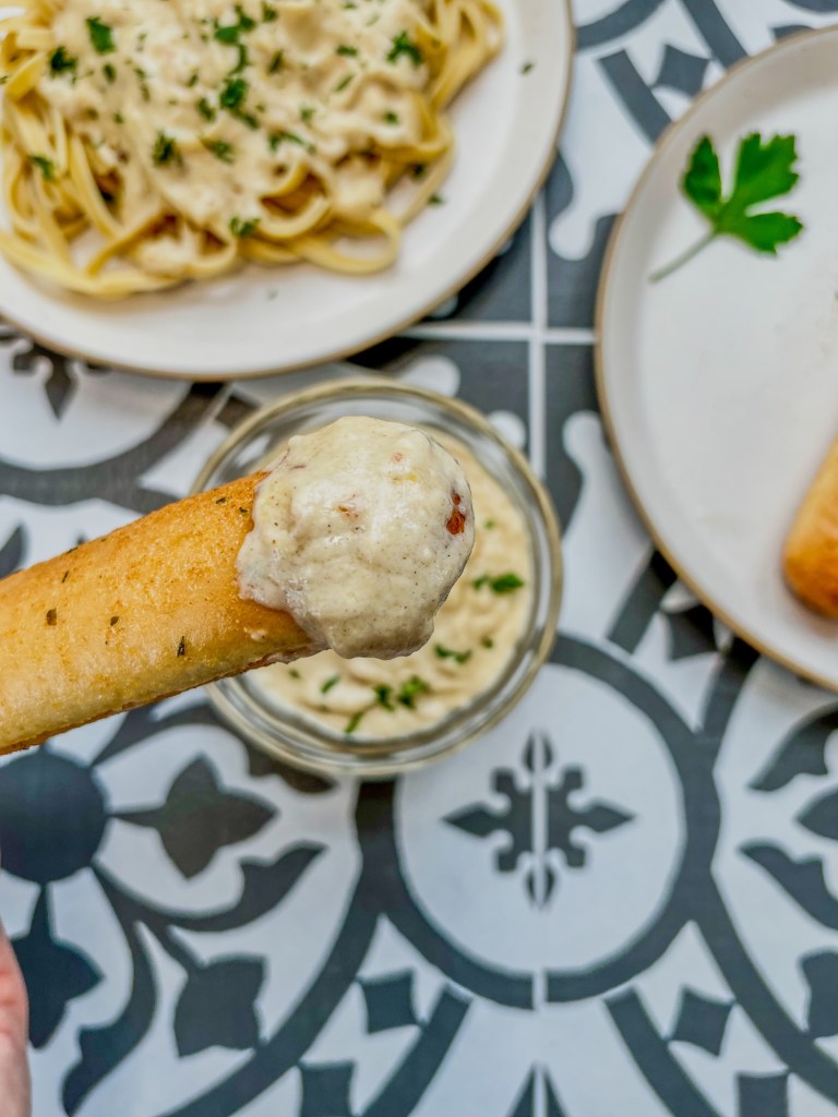 Brown butter alfredo sauce in a dish with a breadstick that's just been freshly dipped in it