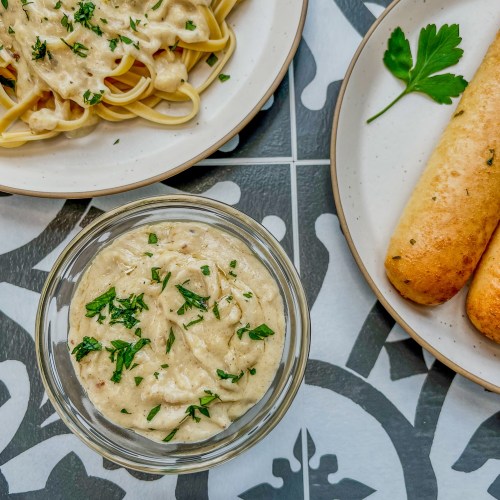 Brown butter alfredo sauce in a dish with some breadsticks and a plate of fettuccine off to the side