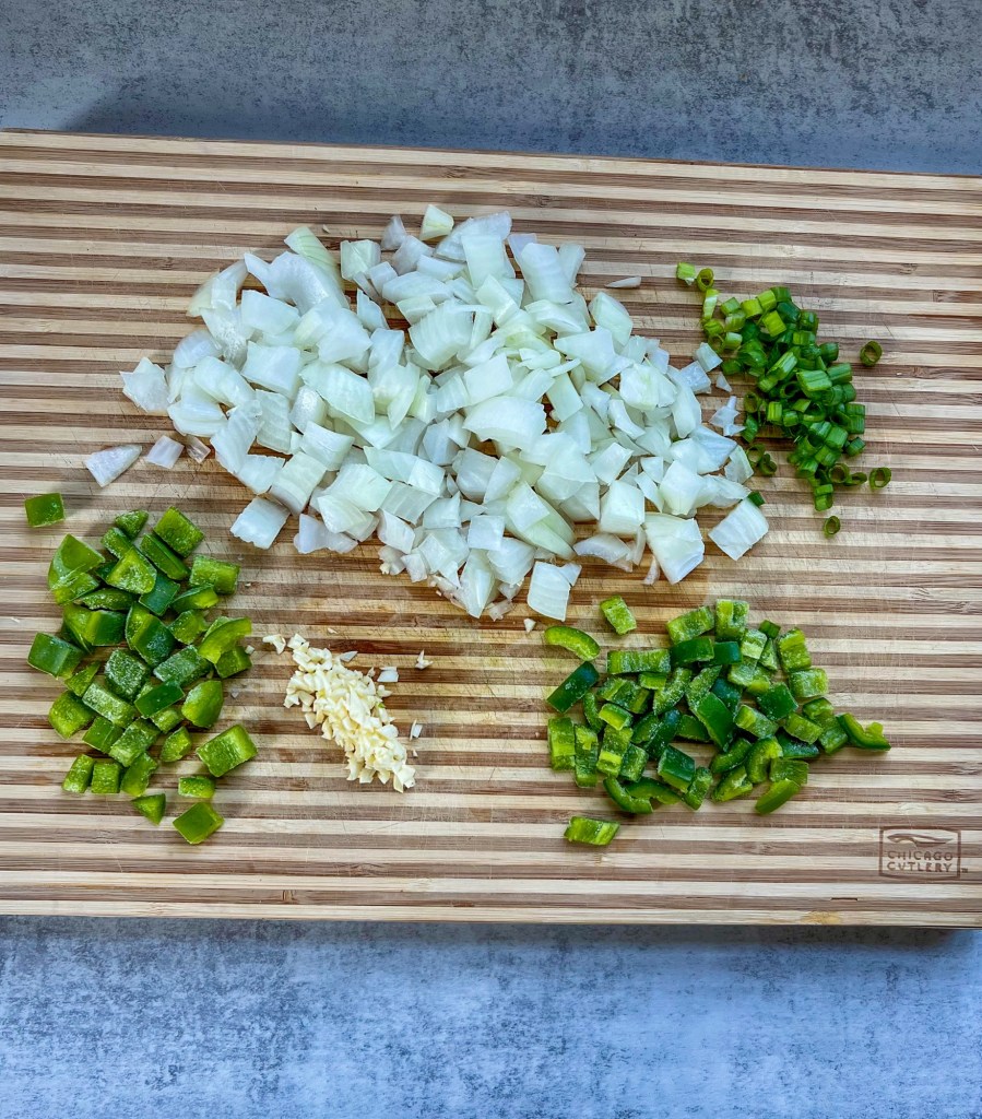 Green onion, jalapeno, yellow onion, garlic, and green pepper cut up on a cutting board