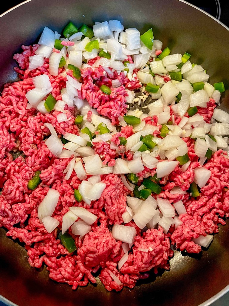 Ground beef and veggies cooking in a large skillet on the stove
