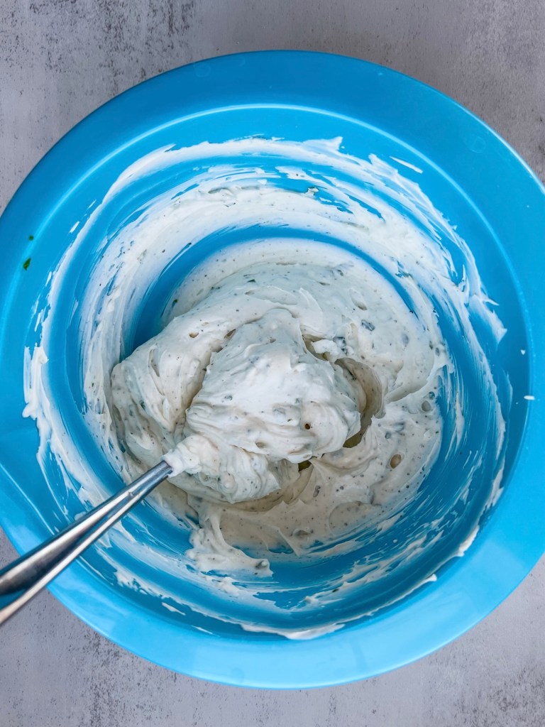 Sour cream and chive spread in a blue mixing bowl with a spoon inside