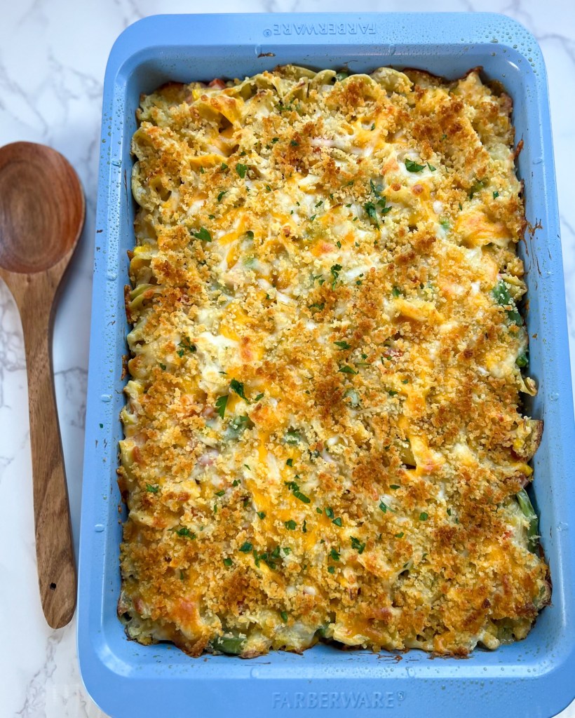 Chicken noodle casserole in a blue pan that just came out of the oven with a wooden spoon next to it