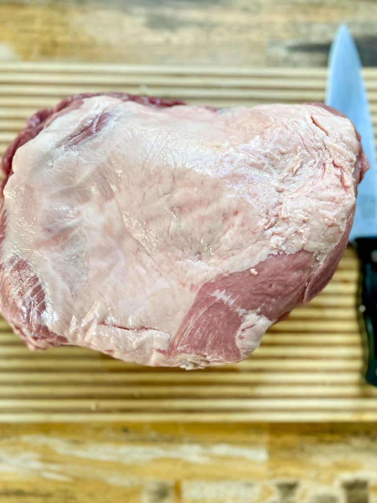 A large raw pork butt on a wooden cutting board with a knife nearby
