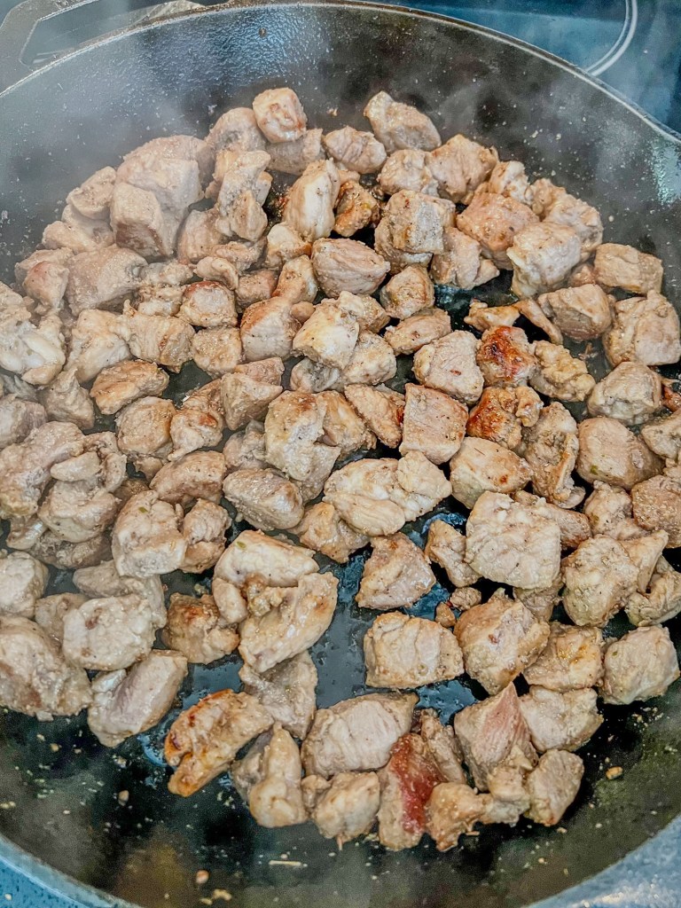 Pork cut up into pieces cooking in a cast iron skillet