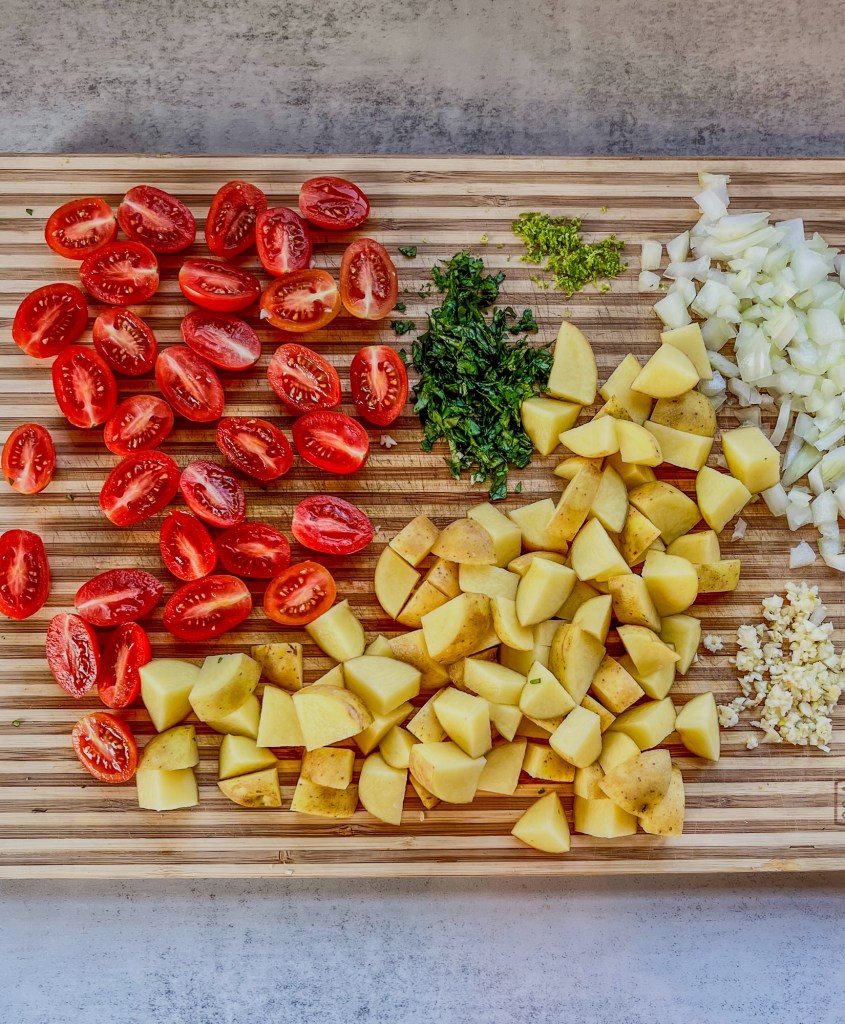 Potatoes, tomatoes, onion, garlic, cilantro, and lime zest all prepped and ready on a wooden cutting board
